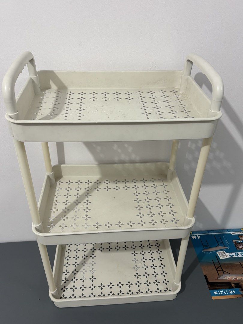3-tier plastic utility storage rack with handles (Category: Storage Boxes & Baskets) located in Manila. Submitted by safefire.ae92b7 (Listing ID 1469357889, Image 1). Description: - Color/Material: Beige plastic - Tiers: 3 shelves with open design and geometric cut-out patterns - Mobility: Built-in top handles for easy pulling and moving - Type: Lightweight, freestanding organizer unit - Best for: Extra storage in bathrooms, kitchens, and laundry