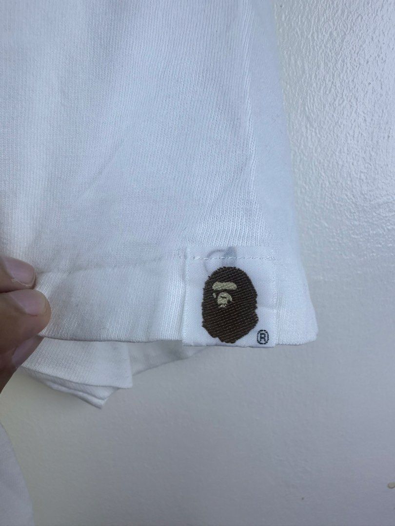 A Bathing Ape Baby Milo Ape Shall Never Kill Ape Tee (Category: Tshirts & Polo Shirts ) located in Manila. Submitted by declutterpromax (Listing ID 1469222173, Image 2). Description: - Color: Clean white with iconic front graphic - Design: Classic 'Ape Shall Never Kill Ape' print - Details: Signature Bape sleeve tag on left cuff and gray size neck tag - Fit: Short sleeves with a comfortable round collar.