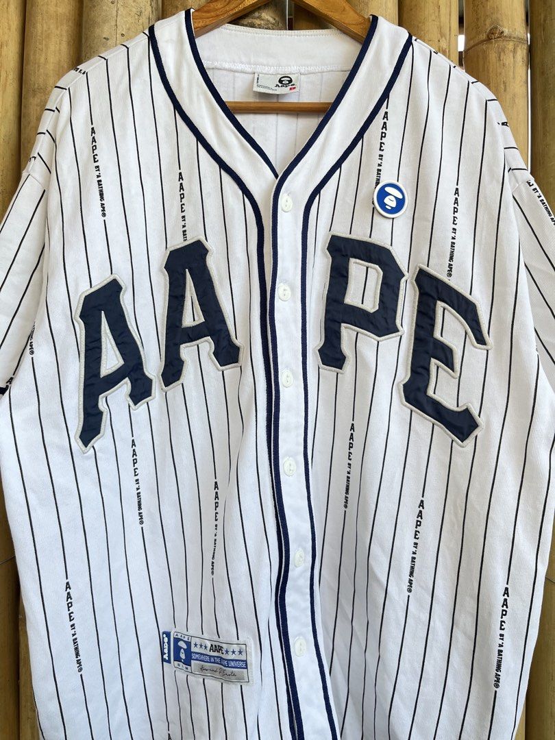 Aape By A Bathing Ape Pinstripe Baseball Jersey (Category: Tshirts & Polo Shirts ) located in Manila. Submitted by thrifttika (Listing ID 1469222530, Image 2). Description: - Brand: Aape by A Bathing Ape - Style: White baseball jersey with navy blue pinstripes - Details: Large raised AAPE chest lettering, button-down front with branded buttons, and woven lower front patch - Size: Large - Condition: Clean, flawless and ready to wear.