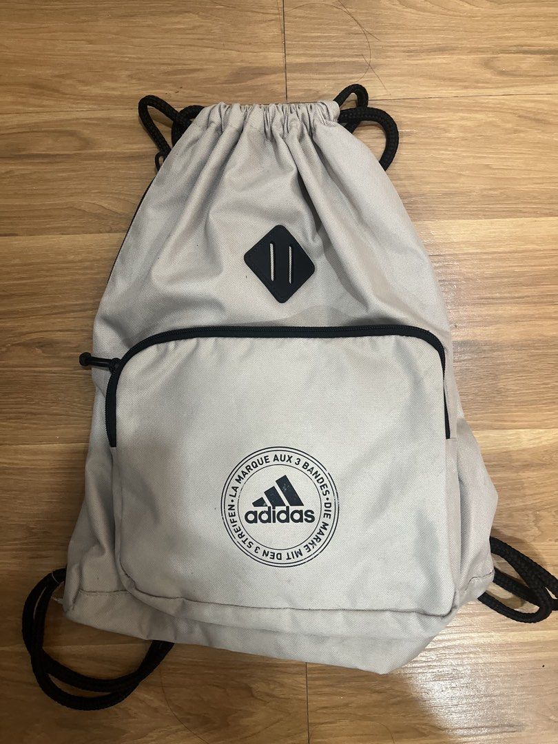 Adidas Drawstring Bag Off White Gym Sack (Category: Backpacks) located in San Fernando. Submitted by nathan_pasahol (Listing ID 1469254325, Image 1). Description: - Brand: Adidas - Color: Off-white with black cord straps - Features: Front zip pocket with circular Adidas logo patch & diamond-shaped lash tab accent - Condition: Clean interior, sturdy rope drawstrings, with faint dirt smudges near the bottom backside - Perfect for daily use, gym, or