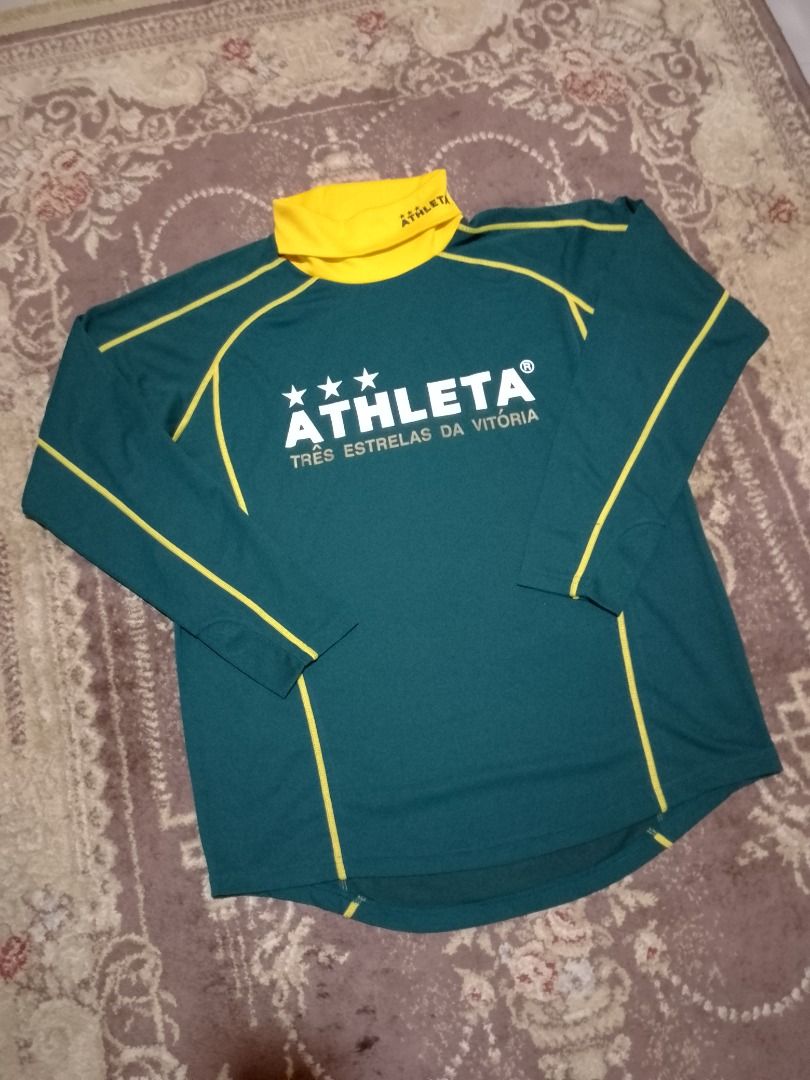 Athleta Long Sleeve Turtle Neck Track Jersey Top (Category: Activewear) located in Bayombong. Submitted by daily10 (Listing ID 1469193739, Image 2). Description: - Brand: Athleta - Size: Large - Dimensions: 22" x 27" - Color: Dark green with yellow turtleneck and contrast stitching - Front Details: Large white Athleta branding, three stars, and Portuguese text - Back Details: Soccer ball graphic with 'Marca Brasileira' and 'Café do Brasil' - Cond