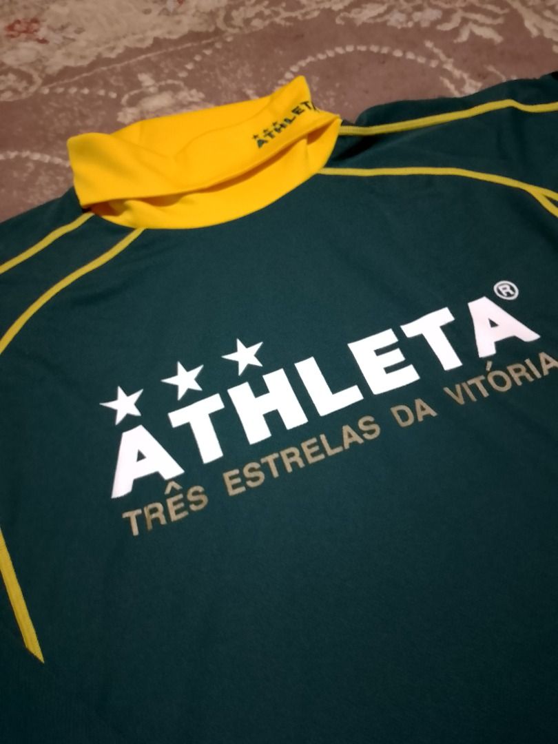 Athleta Long Sleeve Turtle Neck Track Jersey Top (Category: Activewear) located in Bayombong. Submitted by daily10 (Listing ID 1469193739, Image 3). Description: - Brand: Athleta - Size: Large - Dimensions: 22" x 27" - Color: Dark green with yellow turtleneck and contrast stitching - Front Details: Large white Athleta branding, three stars, and Portuguese text - Back Details: Soccer ball graphic with 'Marca Brasileira' and 'Café do Brasil' - Cond