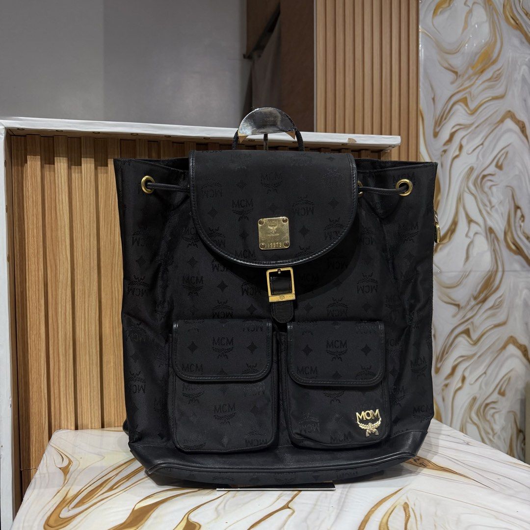 Authentic MCM Black Monogram Nylon Backpack München (Category: Backpacks) located in Bambang. Submitted by heats777 (Listing ID 1469169876, Image 1). Description: - Brand: MCM - Material: Black monogram fabric with leather trim - Hardware: Gold-tone with minor scuffs - Closure: Drawstring under main flap with buckle - Pockets: Two front utility pockets - Details: Classic MCM metal logo plaque and engraved München serial number plate (13573) - Con