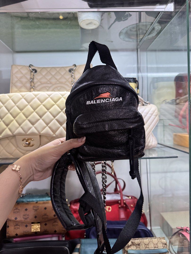 Balenciaga Black Mini Backpack (Category: Backpacks) located in Quezon City. Submitted by derill_shop (Listing ID 1469277059, Image 1). Description: - Brand: Balenciaga - Material: Premium black crinkled leather - Design: White brand lettering with bold red graphic logo on front zipper pocket - Straps: Adjustable black nylon shoulder straps with sleek clip hardware - Features: Convenient top carry handle and front pocket storage - Style: Compact,