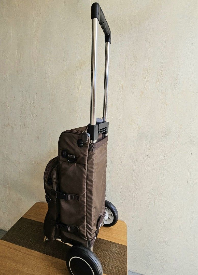 Brown Rolling Trolley Bag with Extendable Handle and Wheels (Category: Luggage) located in Meycauayan. Submitted by amazinggrace_143 (Listing ID 1469291272, Image 3). Description: - Color: Brown - Features: Extendable metal handle, sturdy rolling wheels, and a metal support stand to keep it upright - Storage: Detachable smaller front pouch with zipper, side pockets, and compression straps with buckles - Condition: Clean fabric body, smooth-glidin