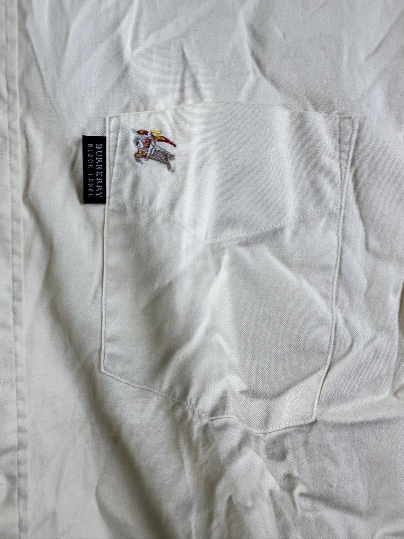 Burberry Black Label Short Sleeve Button Down Shirt Cream (Category: Shirts) located in Manila. Submitted by declutterpromax (Listing ID 1469214621, Image 2). Description: - Authentic Burberry Black Label short-sleeve button-down shirt in a versatile cream color - Features a classic collar, front button closure, and a single chest pocket with embroidered equestrian knight logo and branded tag - Stylish Nova check pattern lining inside the collar 