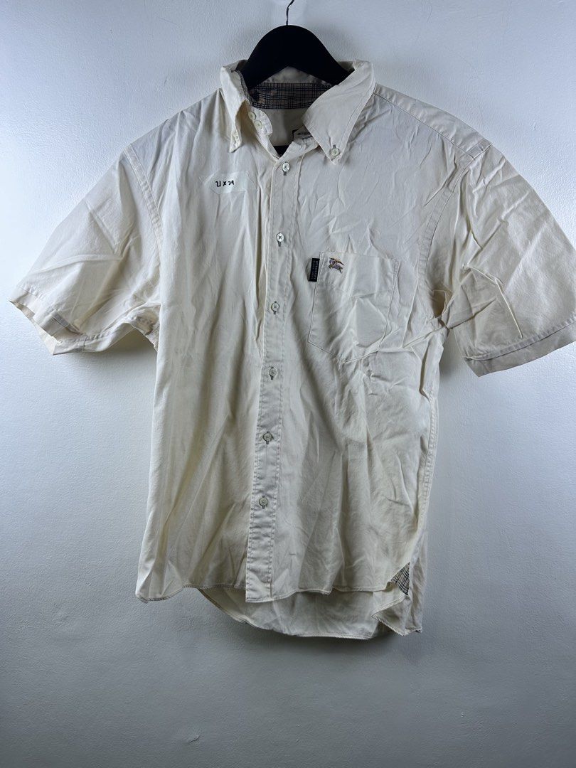 Burberry Black Label Short Sleeve Button Down Shirt Cream (Category: Shirts) located in Manila. Submitted by declutterpromax (Listing ID 1469214621, Image 1). Description: - Authentic Burberry Black Label short-sleeve button-down shirt in a versatile cream color - Features a classic collar, front button closure, and a single chest pocket with embroidered equestrian knight logo and branded tag - Stylish Nova check pattern lining inside the collar 
