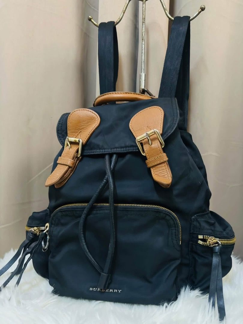 Burberry Nylon & Leather Rucksack (Category: Backpacks) located in Santiago. Submitted by evrythngulove (Listing ID 1469335430, Image 2). Description: Authentic black nylon Burberry backpack featuring chic tan leather trim and gold hardware. Includes a drawstring main compartment, multiple outer zip pockets, and comfortable adjustable straps. Perfect for everyday luxury!.