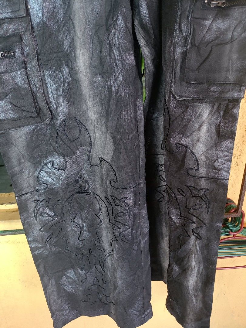 Burfict Black Coated Cargo Pants with Embroidery (Category: Jeans) located in General Mariano Alvarez. Submitted by markaj1699 (Listing ID 1469175817, Image 3). Description: - Brand/Model: Burnin Black Coated Denim Cargo Pants - Wash/Finish: Distressed metallic wash effect for a unique edge - Pockets: Multiple utility pockets equipped with zip details - Detailing: Intricate gothic embroidery on the lower legs - Hardware: Branded metal buttons and
