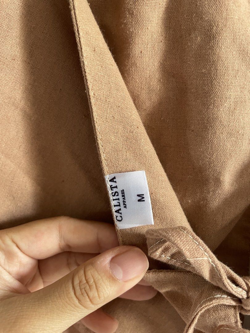 Calista Apparel Brown Halter Top Size M (Category: Sleeveless) located in Agdangan. Submitted by happyphoenix.d92869 (Listing ID 1469210643, Image 3). Description: - Brand: Calista Apparel - Size: M - Color: Brown - Style: Halter top with open back and tie-back ribbon detail at the hem - Material: Textured fabric with structured front panels.