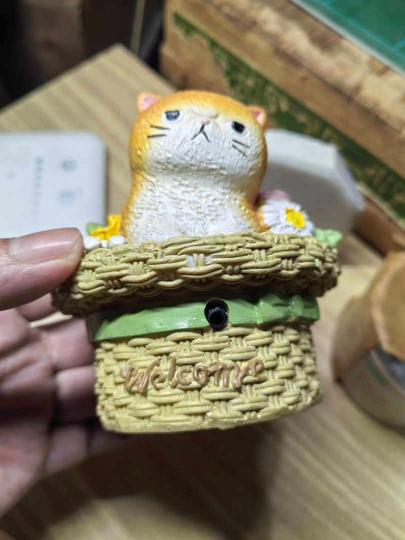 Cat in Flower Basket Welcome Figurine (Category: Other Home Decor) located in Cebu City. Submitted by dudes_villanueva (Listing ID 1469281648, Image 3). Description: Cat in Flower Basket Welcome Figurine / Sound Box Hand-painted novelty decor featuring an adorable grumpy orange tabby cat nestled inside a woven flower basket decorated with roses and daisies. ​Features a "Welcome" script on the front, an electronic sensor/audio module port, and a b
