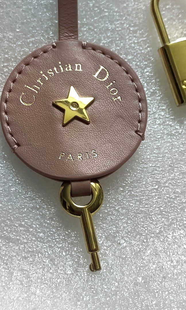 Christian Dior Bag tag with Lock & Key (Category: Luxury Accessories) located in Manila. Submitted by blings_thingies (Listing ID 1469177131, Image 3). Description: • Circular pink leather tag embossed with gold-lettered "Christian Dior" and "Paris", centered with a raised gold-finish star emblem and a matching hanging key. • Accessories: A matching gold-finish padlock featuring the engraved Dior signature..