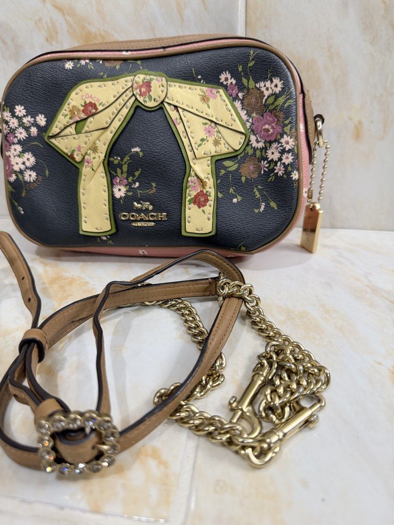 Coach Floral Bow Camera Bag (Category: Luxury Bags & Wallets) located in Manila. Submitted by haveago0dthrift (Listing ID 1469256786, Image 2). Description: - Authentic designer-style black leather camera bag - Eye-catching multicolored floral print with a large front decorative bow - Chic tan leather trim, pink accents, and gold-tone hardware - Versatile styling: comes with an adjustable brown leather strap and a detachable crystal buckle chain 