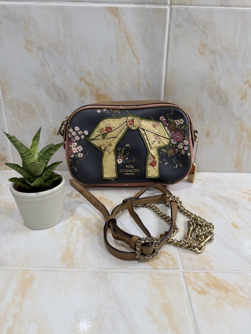 Coach Floral Bow Camera Bag (Category: Luxury Bags & Wallets) located in Manila. Submitted by haveago0dthrift (Listing ID 1469256786, Image 1). Description: - Authentic designer-style black leather camera bag - Eye-catching multicolored floral print with a large front decorative bow - Chic tan leather trim, pink accents, and gold-tone hardware - Versatile styling: comes with an adjustable brown leather strap and a detachable crystal buckle chain 