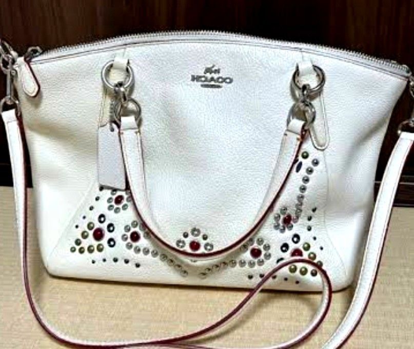 Coach White Leather Satchel Bag with Studs and Strap (Category: Cross-body Bags) located in Manila. Submitted by lene48 (Listing ID 1469170207, Image 2). Description: - Brand: Coach - Color: Off-white - Material: Textured leather with silver-tone hardware - Design: Front embellished with metal studs, grommets, and red stones in floral patterns; clean backside with vertical seam - Closure: Secure zipper top - Carry options: Dual top handles and a 