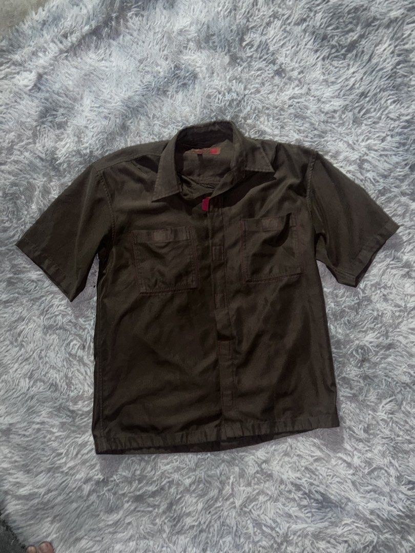 Dark brown short sleeve button-down work shirt with pockets (Category: Shirts) located in Caloocan City. Submitted by sinnr.vault (Listing ID 1469257773, Image 1). Description: - Color: Dark brown - Style: Short sleeve with classic collar and front button closure - Pockets: Two chest utility pockets with button flaps - Fit: Relaxed fit for effortless daily wear - Versatility: Neutral earth tone that pairs easily with any jeans or trousers.