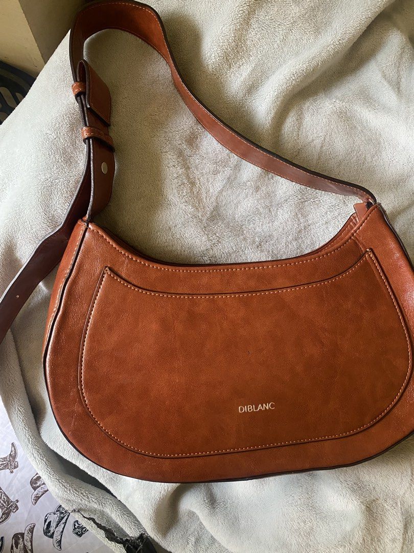 DIBLANC Crescent Shoulder Bag (Category: Shoulder Bags) located in Davao. Submitted by kuromisplace (Listing ID 1469178207, Image 3). Description: DIBLANC faux-leather hobo shoulder bag in a rich tan-brown shade. This Korean boutique brand bag features a structured half-moon shape, a distinctive curved front pocket panel, clean contrast stitching, and a thick adjustable buckled shoulder strap. 📌 sign of use only 📍 Davao City .