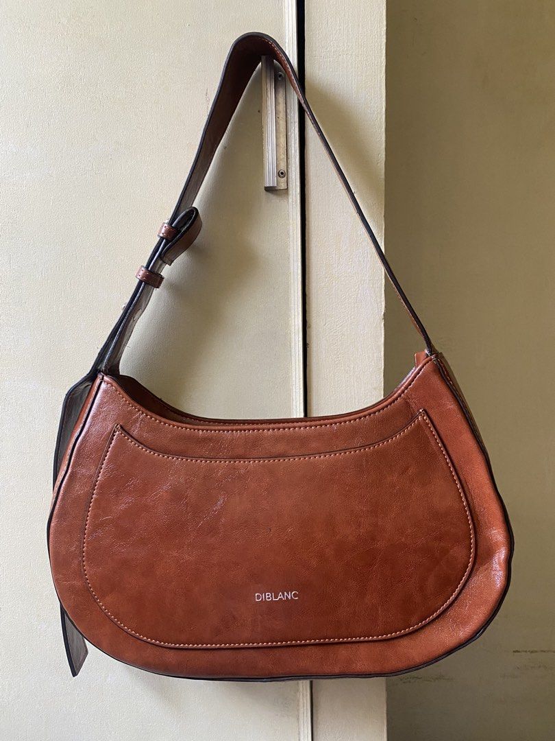 DIBLANC Crescent Shoulder Bag (Category: Shoulder Bags) located in Davao. Submitted by kuromisplace (Listing ID 1469178207, Image 1). Description: DIBLANC faux-leather hobo shoulder bag in a rich tan-brown shade. This Korean boutique brand bag features a structured half-moon shape, a distinctive curved front pocket panel, clean contrast stitching, and a thick adjustable buckled shoulder strap. 📌 sign of use only 📍 Davao City .