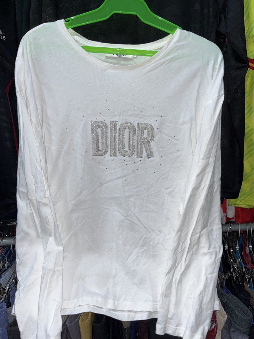 Dior Long Sleeve Crystal Logo Tee (Category: Longsleeves) located in Tabuk. Submitted by collectors_thrift_shop (Listing ID 1469168412, Image 2). Description: - Brand: Dior - Color: White - Size: 13 - Material: Comfortable cotton - Design: Textured Dior lettering on the chest with crystal embellishments and a classic round neckline - Condition: Clean with no major stains or flaws - Style: Great everyday layering piece.