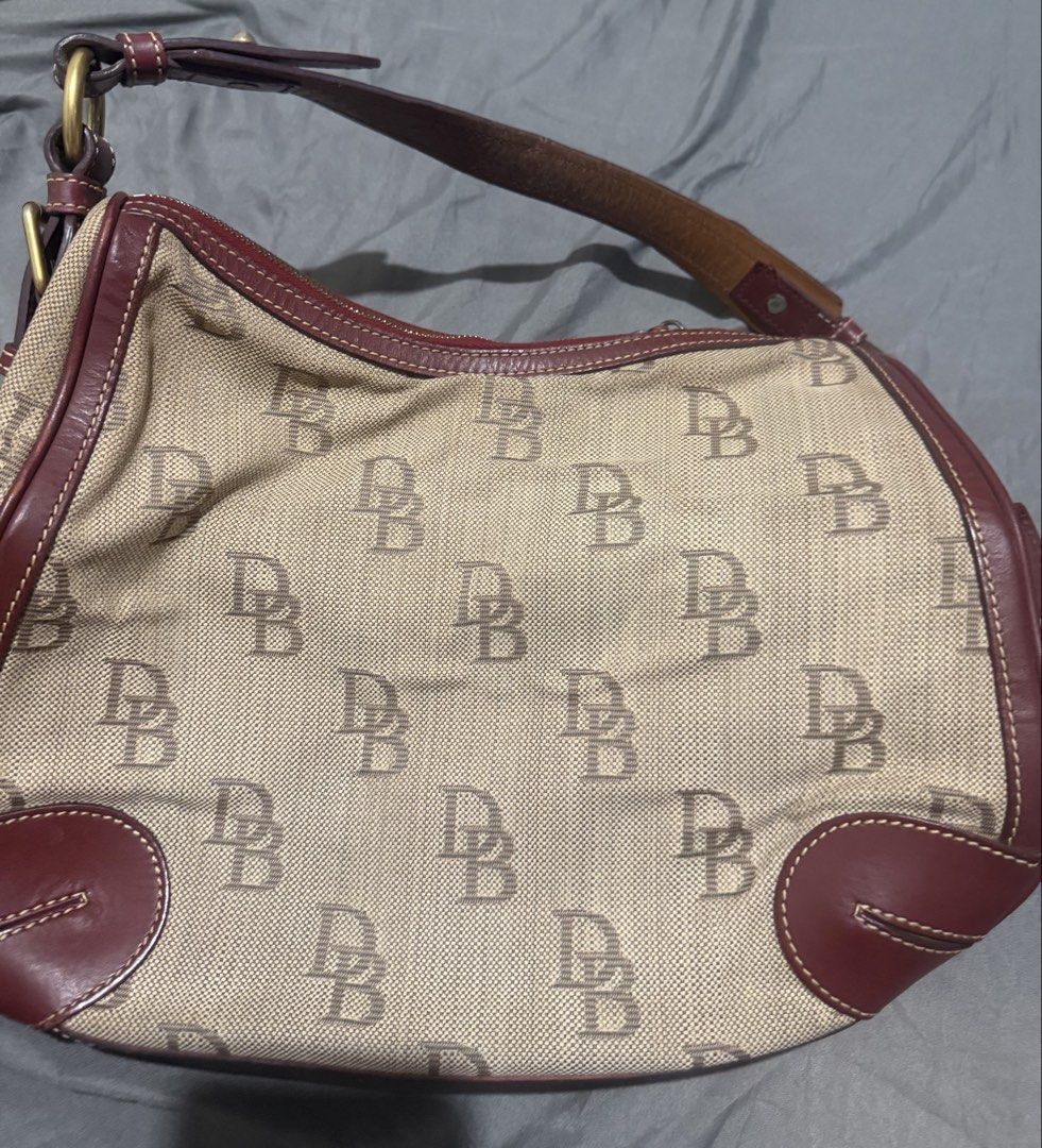 Dooney & Bourke Monogram Shoulder Bag Brown (Category: Luxury Bags & Wallets) located in Cainta. Submitted by mykee1 (Listing ID 1469228335, Image 2). Description: - Authentic Dooney & Bourke shoulder bag - Tan fabric body with iconic allover DB monogram print - Dark brown leather trim and single adjustable strap - Secure zip top closure with brass-tone hardware - Structured curved base with reinforced leather bottom corners - Classic Y2K early 2