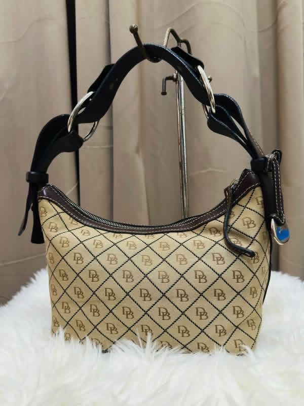 Dooney & Bourke Monogram Shoulder Bag (Category: Luxury Bags & Wallets) located in Santiago. Submitted by evrythngulove (Listing ID 1469334089, Image 1). Description: Authentic Dooney & Bourke shoulder bag in classic beige and brown monogram with dark brown leather trim. Features a top zip closure, clean interior with pockets, and a key keeper strap. Perfect for everyday use!.