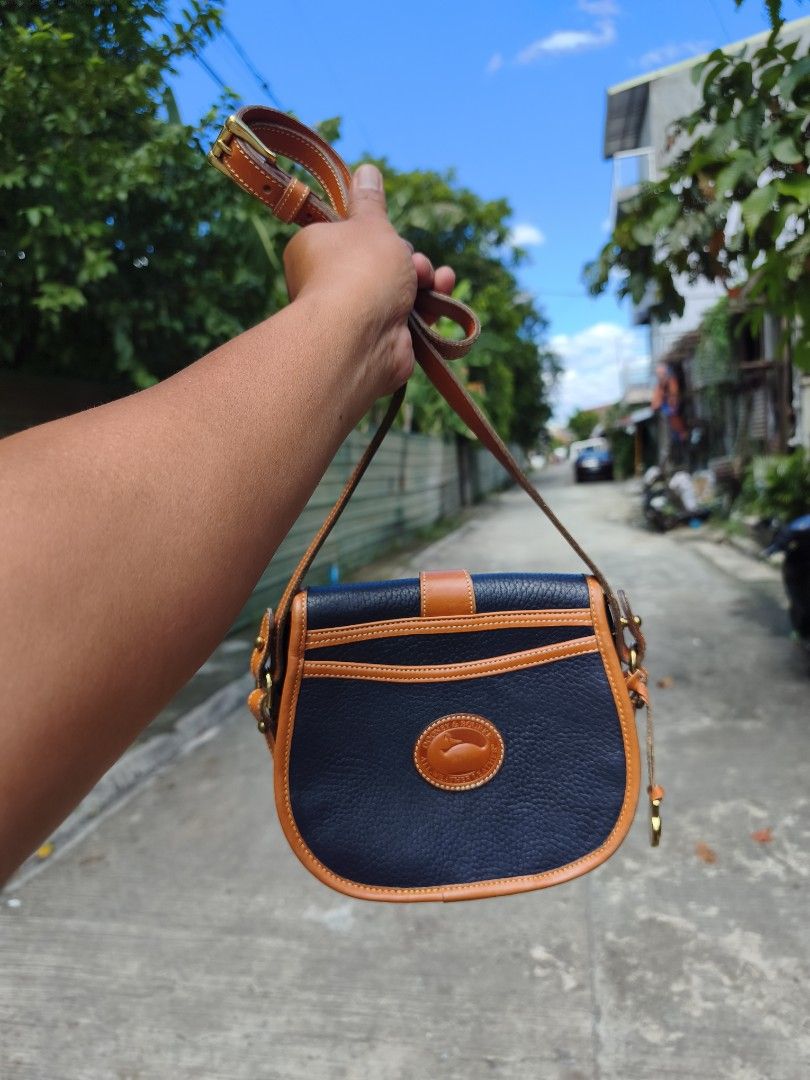 Dooney & Bourke Vintage Leather Saddle Bag (Category: Luxury Bags & Wallets) located in Bulacan. Submitted by THA_D_THRIFT (Listing ID 1469198732, Image 1). Description: - Brand: Dooney & Bourke - Material: Textured leather with suede interior - Color: Dark navy with tan trim - Hardware: Brass - Origin: Made in USA - Closure: Front flap with strap and metal loop - Pockets: 1 interior zippered pocket - Strap: Adjustable shoulder/crossbody strap - 