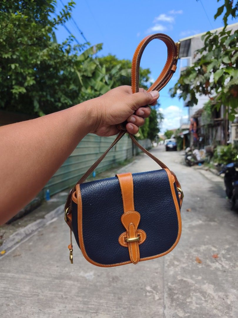 Dooney & Bourke Vintage Leather Saddle Bag (Category: Luxury Bags & Wallets) located in Bulacan. Submitted by THA_D_THRIFT (Listing ID 1469198732, Image 2). Description: - Brand: Dooney & Bourke - Material: Textured leather with suede interior - Color: Dark navy with tan trim - Hardware: Brass - Origin: Made in USA - Closure: Front flap with strap and metal loop - Pockets: 1 interior zippered pocket - Strap: Adjustable shoulder/crossbody strap - 