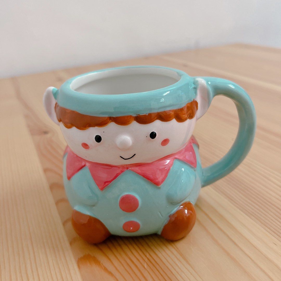 Elf Ceramic Mug (Category: Coffee & Tea Tableware) located in Davao. Submitted by lovedbyhaze (Listing ID 1469247737, Image 1). Description: - Adorable elf-shaped ceramic mug in pastel blue - Features pink collar, red buttons, brown shoes, and painted face - Beautiful glossy finish throughout - Ideal for morning coffee, tea, or hot chocolate - Great decorative piece for your desk or kitchen counter.