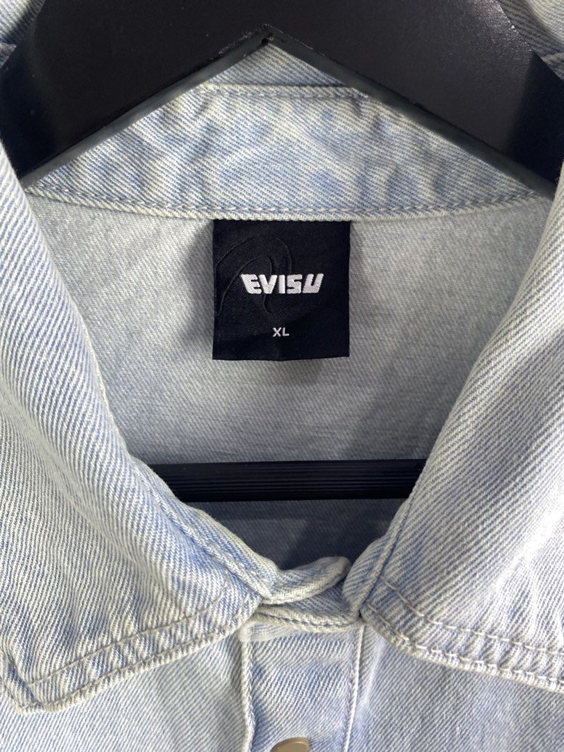 Evisu Light Blue Denim Shirt Size XL (Category: Tshirts & Polo Shirts ) located in Manila. Submitted by declutterpromax (Listing ID 1469289928, Image 2). Description: - Brand: Evisu - Color: Light wash blue - Size: XL - Details: Button-down front with metal snap buttons - Pockets: Dual front chest pockets with iconic embroidered white seagull branding - Hem: Curved hemline design - Authenticity: Crafted with pride tag on the inner collar - Condit