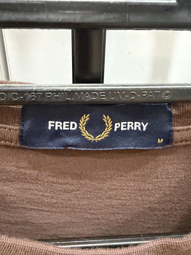 Fred Perry Brown T-Shirt Size M (Category: Tshirts & Polo Shirts ) located in San Pedro. Submitted by tineodulio (Listing ID 1469266275, Image 2). Description: - Brand/Model: Fred Perry T-Shirt - Color: Brown - Size: M - Design: Classic crew neck, short sleeves - Logo: Large black embroidered laurel wreath on the chest - Details: Blue collar tag with gold lettering - Condition: Clean fabric, great basic tee for daily casual wear.