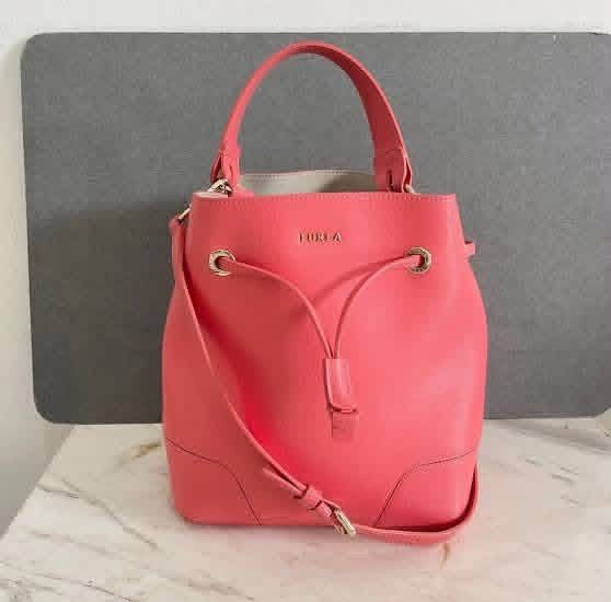 Furla Pink Leather Bucket Bag (Category: Luxury Bags & Wallets) located in Santiago. Submitted by evrythngulove (Listing ID 1469334774, Image 1). Description: pink Furla leather bucket bag with gold-tone hardware. Features a drawstring closure, top handle, adjustable shoulder strap, and unlined interior. Clean condition inside and out. Great everyday size!.