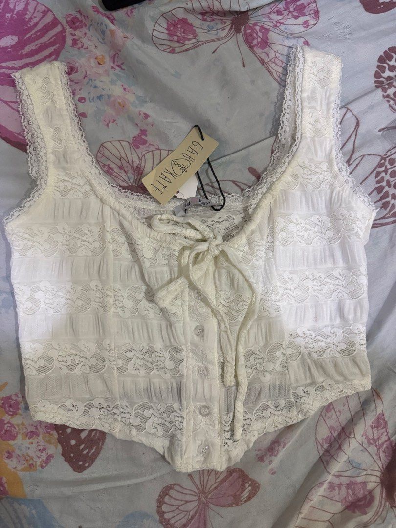 Gab & Kate White Lace Crop Top (Category: Sleeveless) located in Cebu City. Submitted by hotchkisscebu (Listing ID 1469194398, Image 1). Description: - Brand: Gab & Kate - Condition: Brand new with tags (never worn) - Color: White - Style: Fairycore aesthetic, sleeveless crop top with scoop neckline - Details: Front tie string, button closure, sheer fabric with floral lace panels, and scalloped trim.