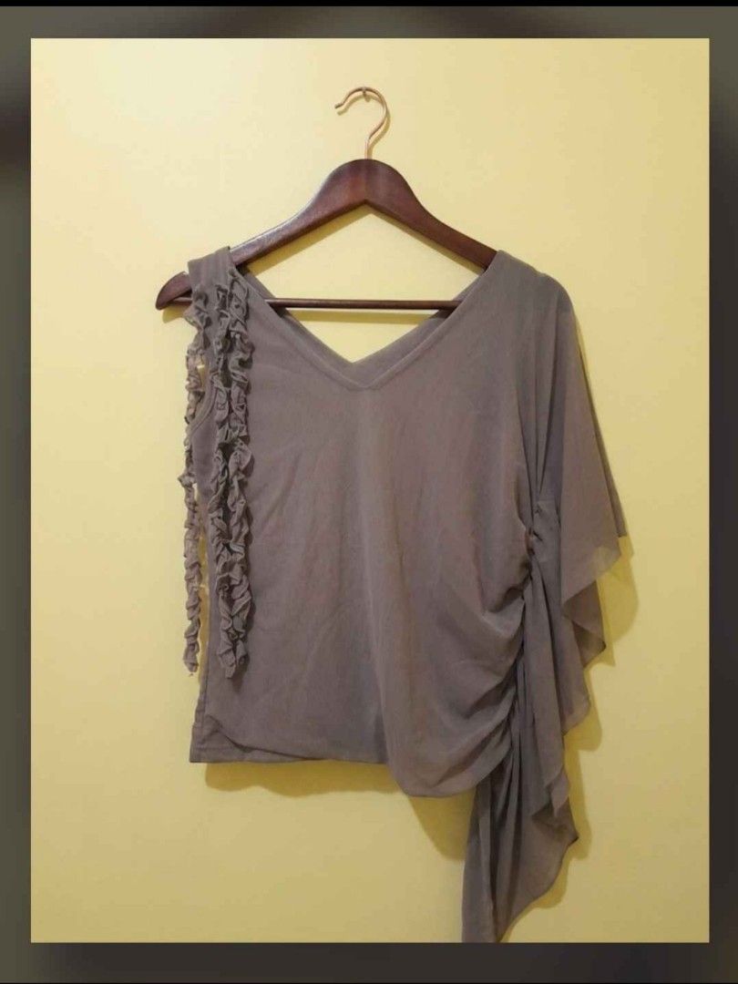 Grey asymmetric drape top with ruffles (Category: Sleeveless) located in Manila. Submitted by seven.vii (Listing ID 1469250557, Image 1). Description: - Color: Grey - Style: Short sleeve blouse with V-neckline - Design: Asymmetrical draped hem and vertical ruffle trim on right shoulder - Material: Lightweight and flowy fabric - Versatility: Easy to pair with skirts or pants for a unique silhouette.