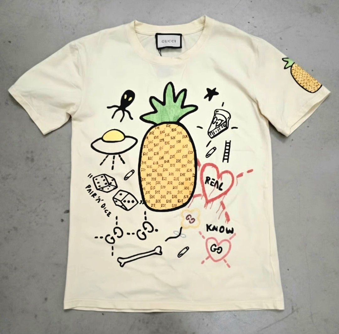 GUCCI "Pineapple & Pair 'N' Dice" Doodle Graphic Tee (Category: Luxury Apparel) located in Pasay City. Submitted by seventhrift.26 (Listing ID 1469280086, Image 1). Description: ​Size: Medium (M) ​Color: Off-White / Light Cream ​Condition: Pre-loved / Good Condition (Please refer to detailed photos for exact condition) ​✨ Features the iconic pineapple GG monogram print with doodle graphics on front and sleeve. Original tags attached. Clean and we