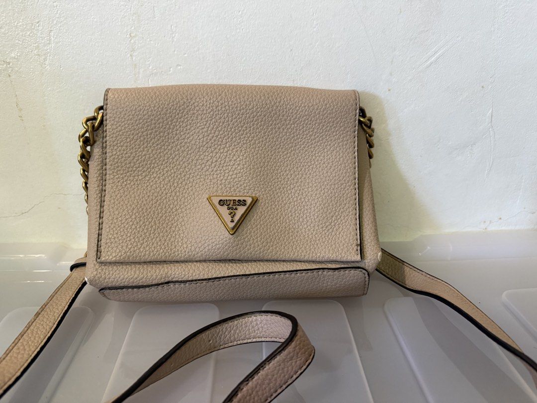 Guess Beige Crossbody Bag with Chain Strap (Category: Cross-body Bags) located in Manila. Submitted by soju2026 (Listing ID 1469163888, Image 1). Description: - Brand: GUESS - Color: Neutral beige - Material: Textured faux leather - Closure: Flap top with iconic metal triangle logo badge - Hardware: Antique brass on chain links - Strap: Adjustable shoulder strap - Interior: Clean lining with a compact main compartment for daily essentials.