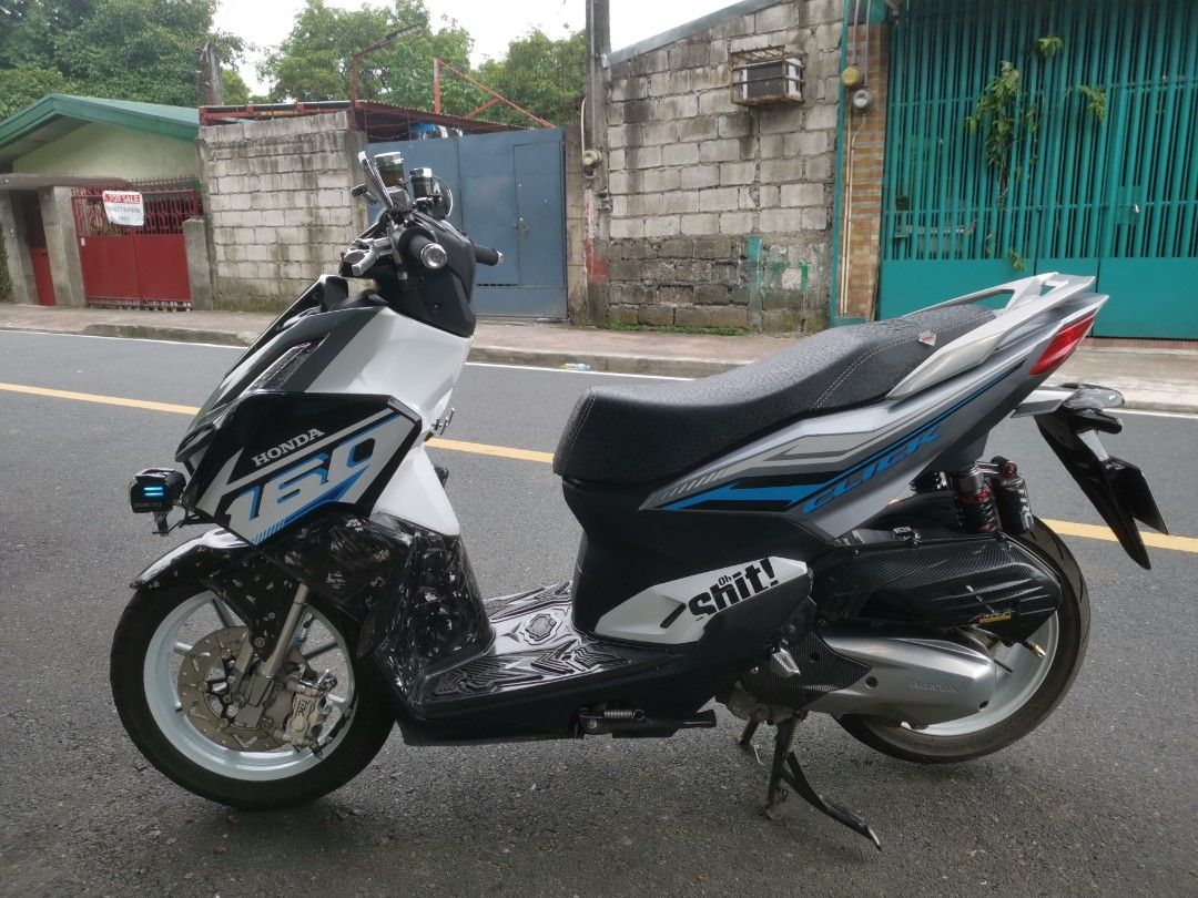 Honda Click 160 Scooter with Custom Upgrades (Category: Motorbikes for Sale) located in Marikina City. Submitted by operoneroal1103 (Listing ID 1469324907, Image 2). Description: Honda Click 160 scooter in white, grey, and black. Custom forged carbon wrap on front panels and exhaust guard. White aftermarket rims and TRC rear suspension installed. Upgraded handlebars, auxiliary fog lights mounted on front forks, and custom seat. Fun decals on the 