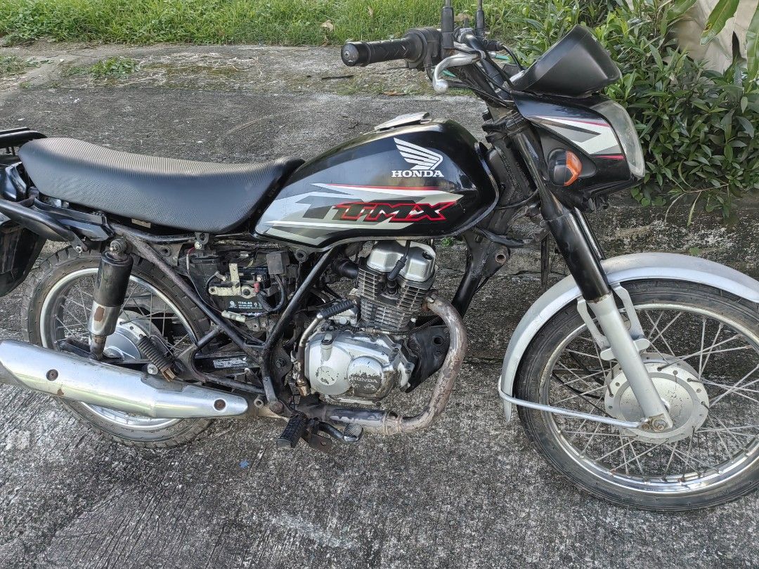 Honda TMX motorcycle (Category: Motorbikes for Sale) located in Silang. Submitted by jamessseller (Listing ID 1469247546, Image 3). Description: Black Honda TMX motorcycle. Manual transmission with standard handlebars and round headlight. Rear cargo rack included, plus registered license plate mounted at the back. Spoke wheels on both front and rear. Frame and exhaust show some rust spots from use. Engine block intact with kick starter..