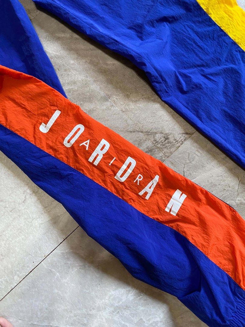 Jordan multi-color nylon track pants (Category: Joggers) located in Butuan. Submitted by jc13thrifts (Listing ID 1469342527, Image 3). Description: - Brand: Jordan - Color: Royal blue with orange and yellow side panels - Details: White 'JORDAN' lettering on left leg, 'MJ23' Nike patch on front thigh - Comfort: Elastic waistband with Jumpman-tipped blue drawstrings - Material: Lightweight nylon with breathable mesh inner lining.