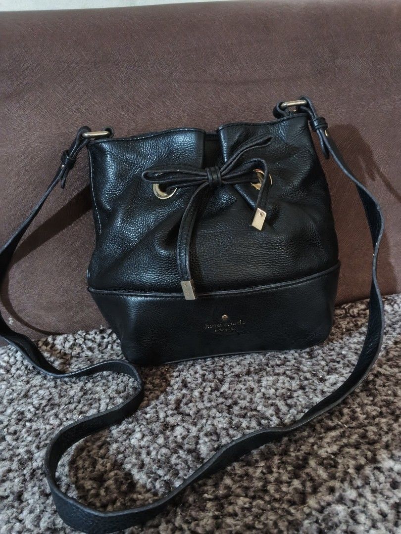 Kate Spade Black Leather Bucket Bag (Category: Luxury Bags & Wallets) located in Bulacan. Submitted by shayneerri02343 (Listing ID 1469173981, Image 1). Description: - Brand: Kate Spade New York - Material: Genuine black pebbled leather with gold-tone hardware - Closure: Drawstring with a stylish front bow detail - Strap: Long, adjustable crossbody strap - Design: Structured base with metallic logo lettering and a clean interior lining - Capacity