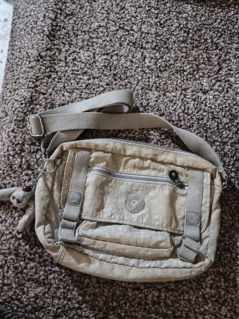 Kipling beige nylon crossbody bag with monkey keychain (Category: Cross-body Bags) located in Bulacan. Submitted by shayneerri02343 (Listing ID 1469189040, Image 1). Description: - Brand: Kipling - Material: Durable nylon - Color: Versatile beige / neutral taupe - Strap: Adjustable for comfortable wear - Exterior: Front flap pocket, zipper pocket, and circular logo patch - Interior: Secure zip closure main compartment, inner zipper pocket, and op