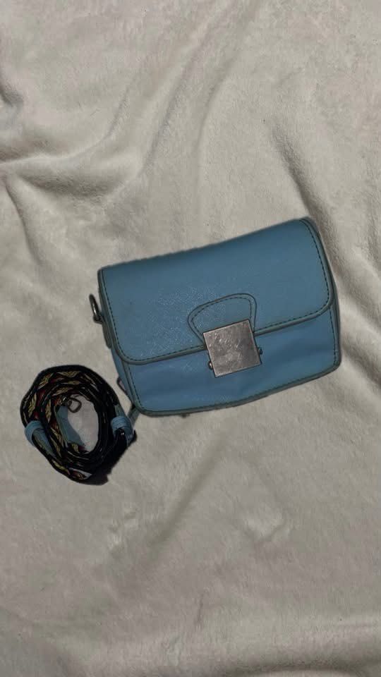 Light blue crossbody bag with decorative strap (Category: Cross-body Bags) located in Manila. Submitted by nobleowl-8fff (Listing ID 1469291017, Image 1). Description: - Color: Light blue - Closure: Square metal clasp - Straps: Includes standard strap plus an extra patterned strap with geometric designs (black, red, yellow) - Size: Compact everyday purse - Condition: Minor wear on metal hardware from regular handling - Perfect for adding a pop of