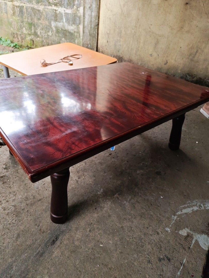 Low table japan surplus (Category: Tables & Sets) located in Manila. Submitted by aks_japansurplus30 (Listing ID 1469200144, Image 1). Description: - Type: Low wooden table / Floor seating table - Finish: Glossy reddish woodgrain top with smooth rounded edges - Legs: Dark brown turned legs with foldable metal brackets for easy storage - Condition: Sturdy and stable, with minor wear around the corner edges - Ideal for: Low living room setups, coff