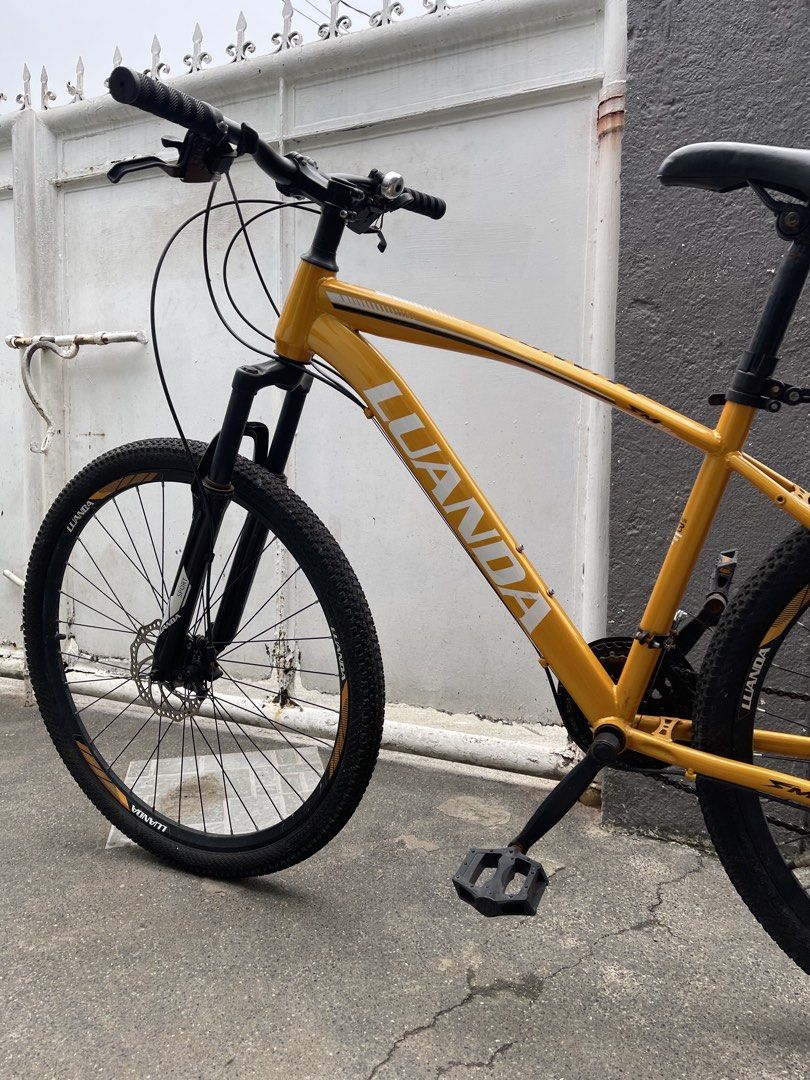Luanda Mountain Bike Yellow (Category: Bicycles) located in Paranaque City. Submitted by cheskadejon (Listing ID 1469213183, Image 3). Description: - Bike: Yellow Luanda mountain bike - Brakes & Suspension: Front suspension fork and reliable disc brakes - Tires & Build: Rugged tires with a solid, functional frame featuring white branding - Extras included: Rear mudguard, kickstand, comfortable handlebar grips, and a small bell - Condition: Overal