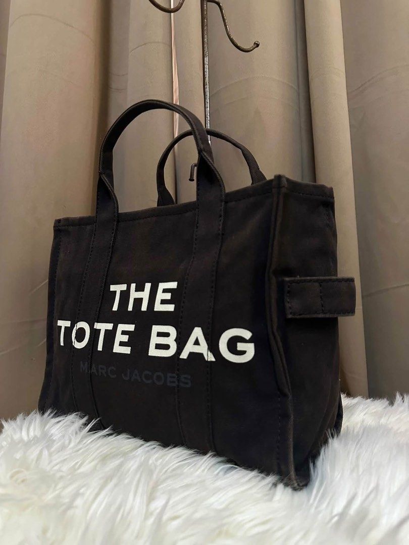 Marc Jacobs The Tote Bag Black Canvas (Category: Tote Bags) located in Lipa City. Submitted by thyra06 (Listing ID 1469290365, Image 2). Description: - Authentic Marc Jacobs black canvas tote bag - Bold white typography on the front with subtle brand lettering - Structured shape with dual top handles - Secure zip-top closure - Spacious interior featuring fabric lining and slip pockets - Neutral color that matches any outfit perfectly - Ideal for 