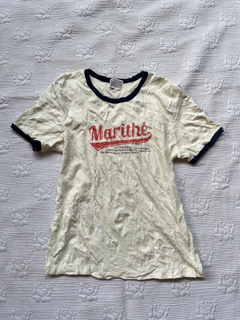Marithe Francois Girbaud Ringer T-Shirt (Category: Tshirts & Polo Shirts ) located in Alabel. Submitted by geragarhea13830 (Listing ID 1469318294, Image 1). Description: - Brand: Marithé François Girbaud - Color: Cream with dark blue contrast trim - Design: Bold red 'Marithé' graphic logo with French text - Fit: Classic fit, short sleeves - Detail: Woven brand label inside neckline - Condition: Good, with natural storage wrinkles.