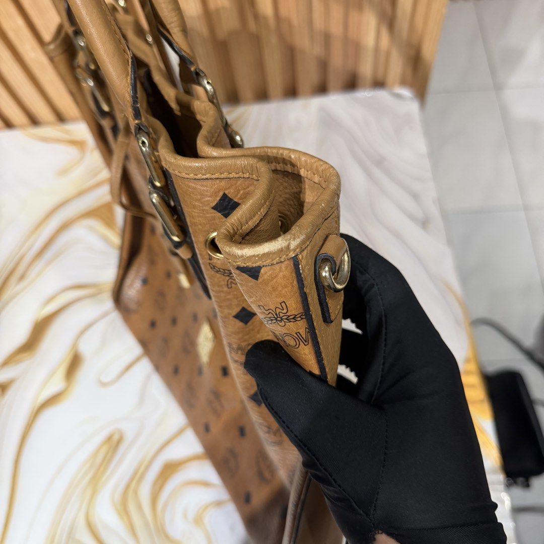 MCM Visetos Brown Monogram Tote Bag (Category: Luxury Bags & Wallets) located in Bambang. Submitted by heats777 (Listing ID 1469169865, Image 3). Description: - Authentic brown MCM Visetos monogram tote bag - Tan leather trim and polished gold-tone hardware - Practical drawstring closure at the front - Double top handles with adjustable buckles - Roomy interior, perfect for daily use - Condition: Regular wear along edges and scuff marks on the bo