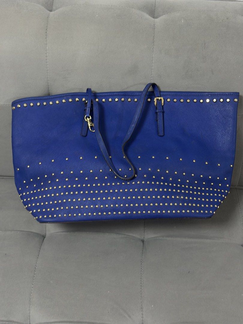 Michael Kors Blue Studded Tote Bag (Category: Tote Bags) located in Tarlac. Submitted by via_banana (Listing ID 1469198274, Image 2). Description: - Brand: Michael Kors - Color: Royal blue with striking gold hardware - Design: Accented with gold studs along the top rim and bottom half - Straps: Dual shoulder straps with buckle adjustments - Extras: Includes classic hanging MK circle charm and gold foil front logo - Interior: Spacious design, perf