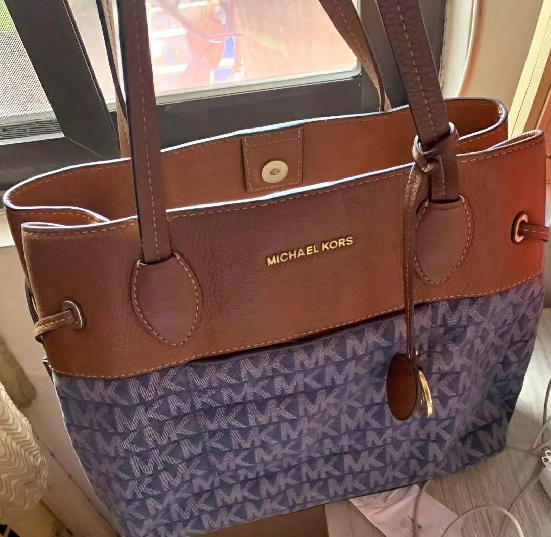 Michael kors mk large denim tote bag (Category: Tote Bags) located in Manila. Submitted by onlinesmartshopping12 (Listing ID 1469380053, Image 2). Description: Stylish Michael Kors tote bag featuring a blue MK monogram pattern with brown leather accents. It has double top handles and a drawstring closure. The interior includes multiple pockets for organization. The bag has a gold-tone MK logo on the front and protective feet on the bottom..