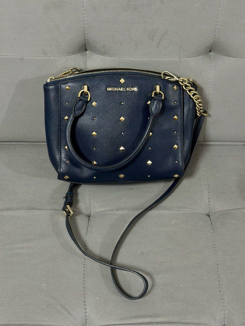 Michael Kors Navy Blue Studded Handbag (Category: Luxury Bags & Wallets) located in Tarlac. Submitted by via_banana (Listing ID 1469198394, Image 1). Description: - Brand: Michael Kors - Color: Navy blue with premium gold hardware - Design: Chic front studded details and a stylish chain link accent on one side - Carry Options: Double top handles and a convenient detachable shoulder strap - Closure: Secure top zipper closure - Interior: Clean fabr