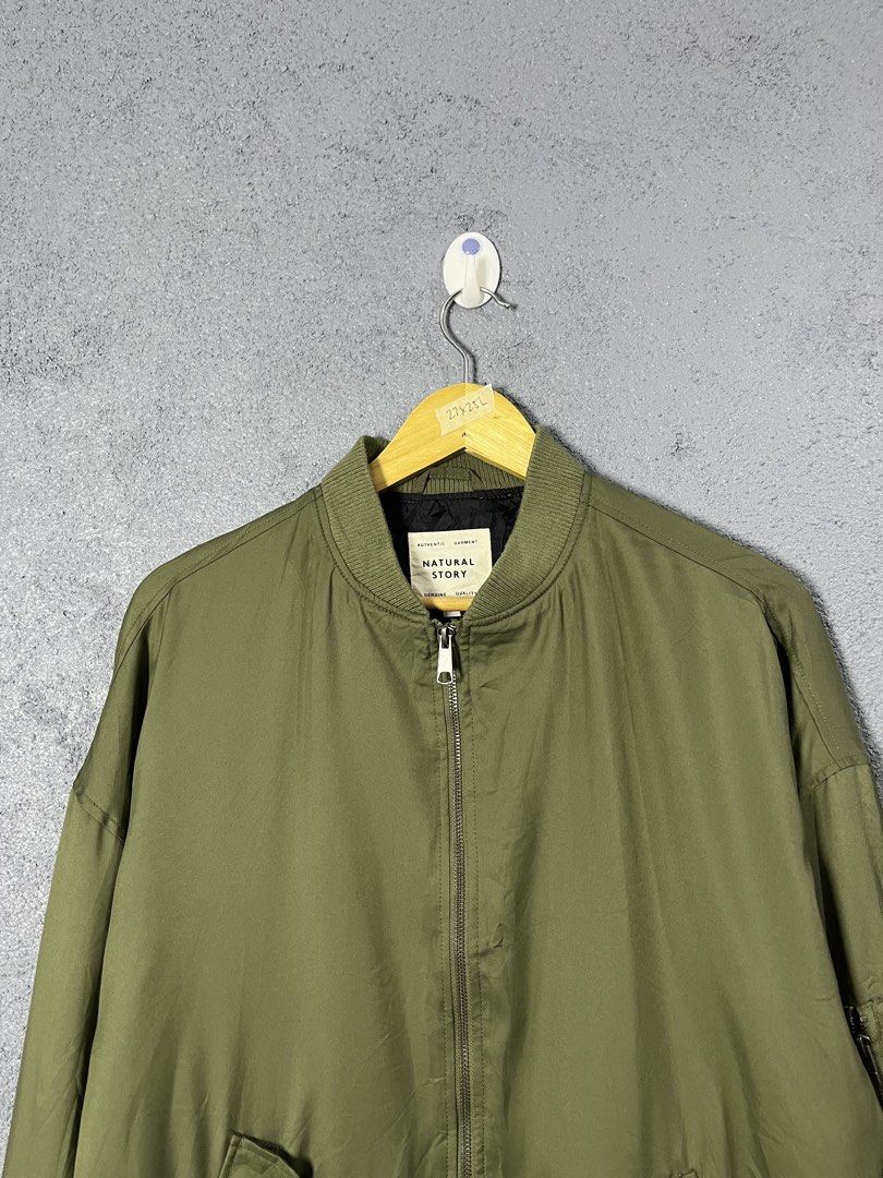 Natural Story Olive Green Bomber Jacket (Category: Coats, Jackets and Outerwear) located in Famy. Submitted by basicthrifted (Listing ID 1469236142, Image 2). Description: - Brand: Natural Story - Color: Olive green with black inner lining - Material: 100% Polyester - Closure: Full front zip - Details: Ribbed collar, cuffs, and hem - Pockets: Utility zipper pocket on the left sleeve and two slanted front pockets - Condition: Excellent.